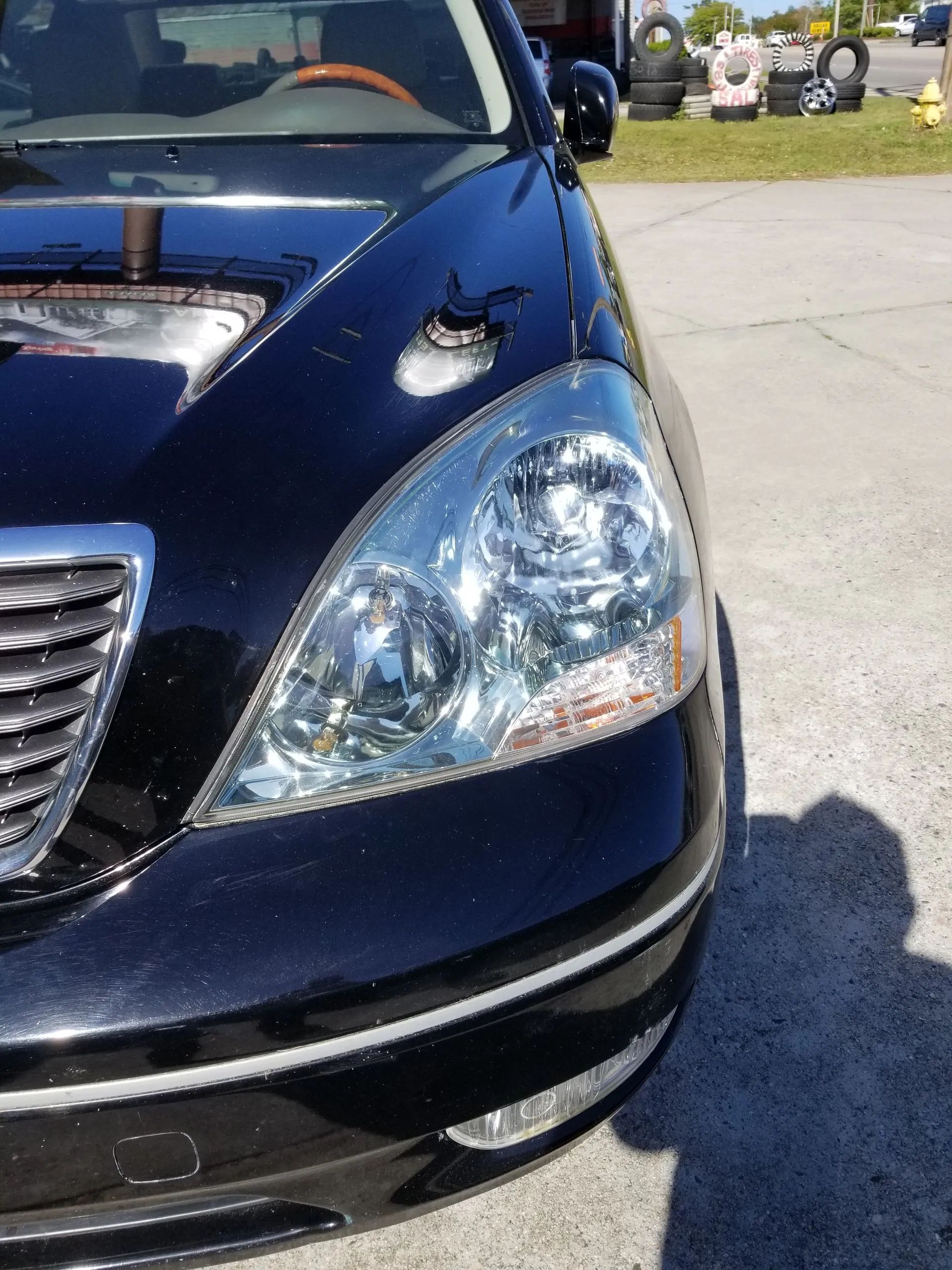 Black Lexus car's front with a damaged hood and headlight, parked outdoors.