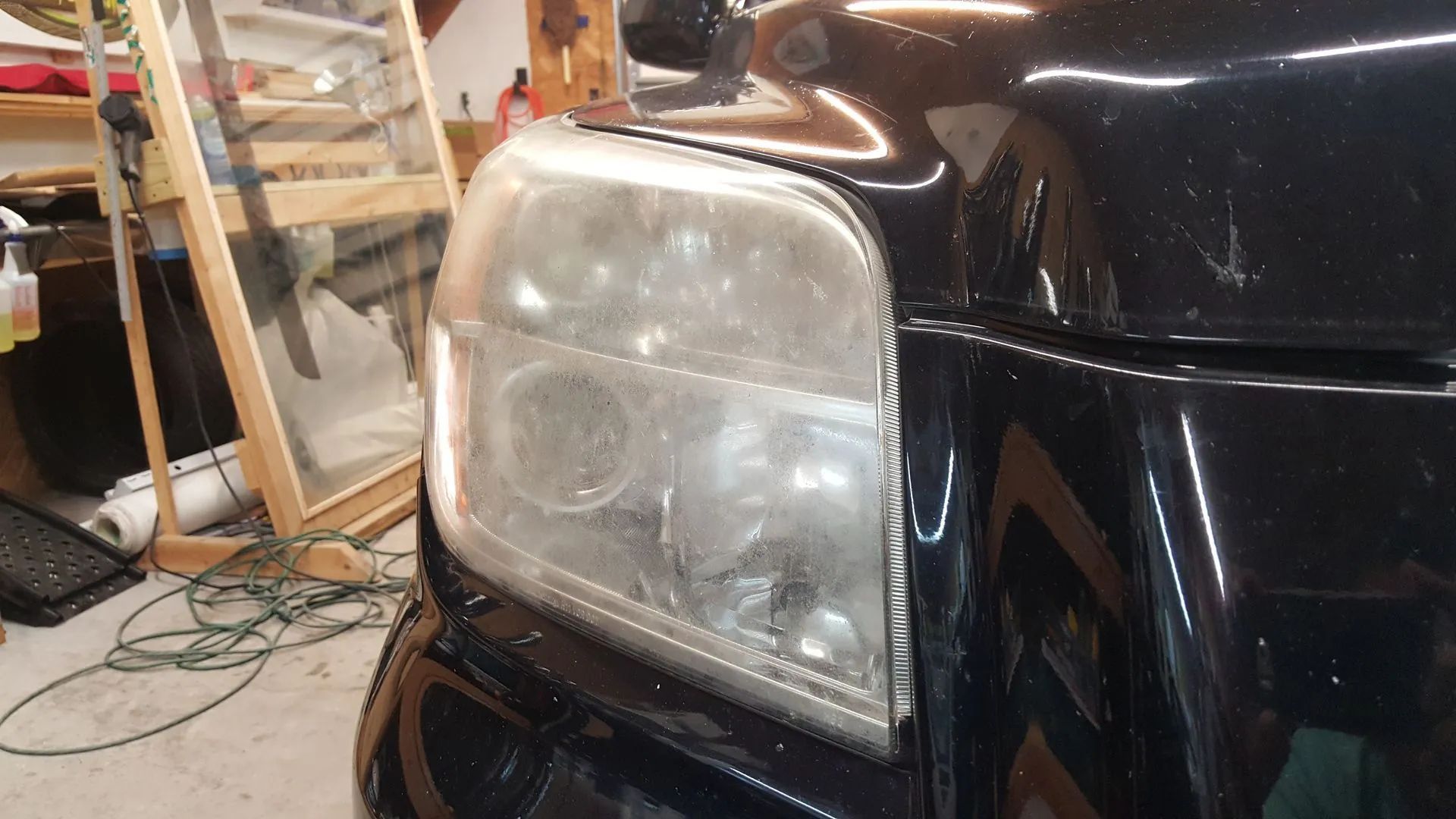 A cloudy car headlight on a black vehicle.