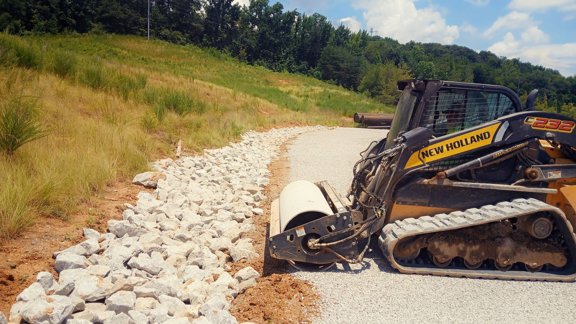 A new holland tractor is working on a gravel road.