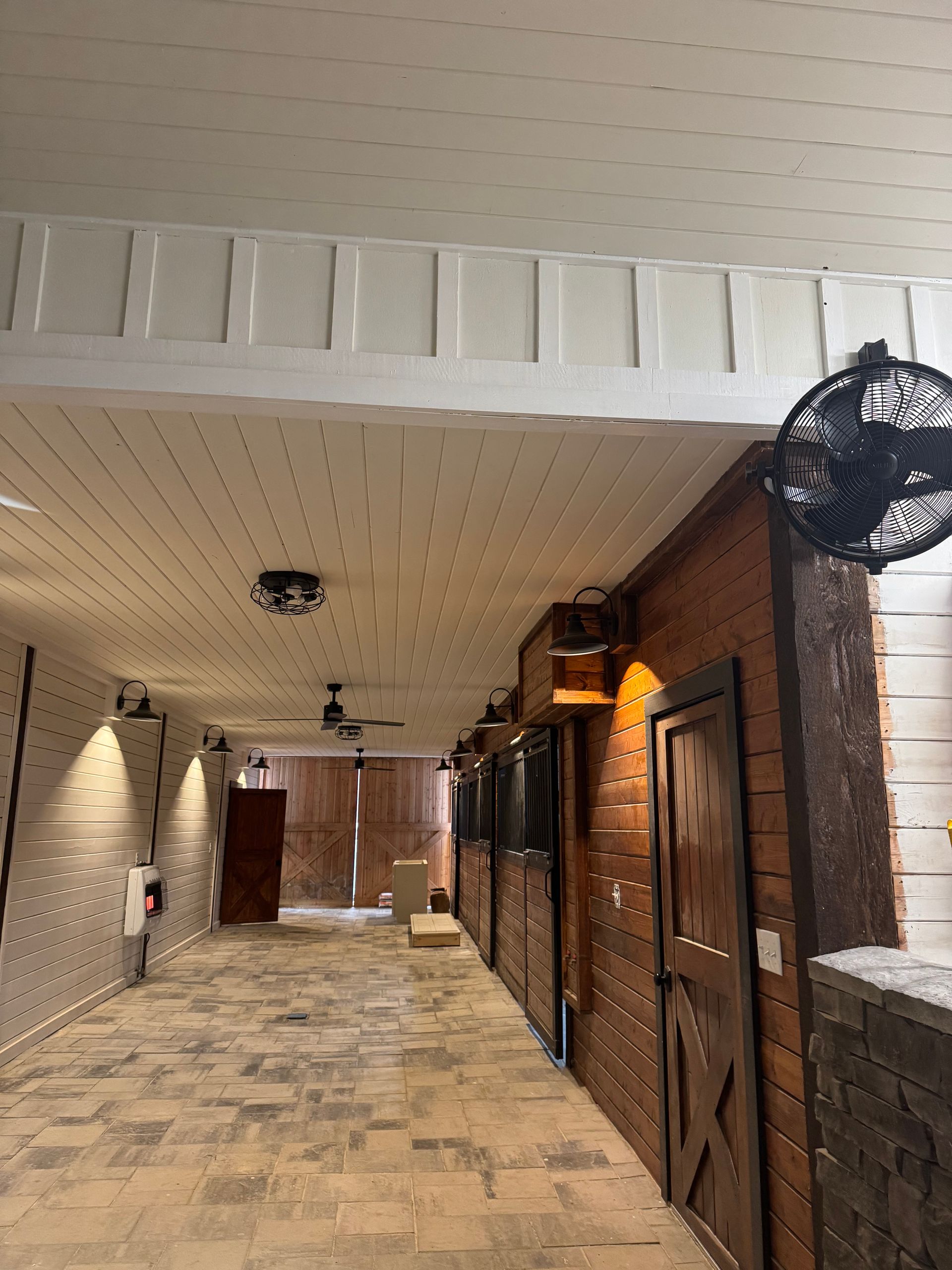 A long hallway with brick walls and a fan on the wall.