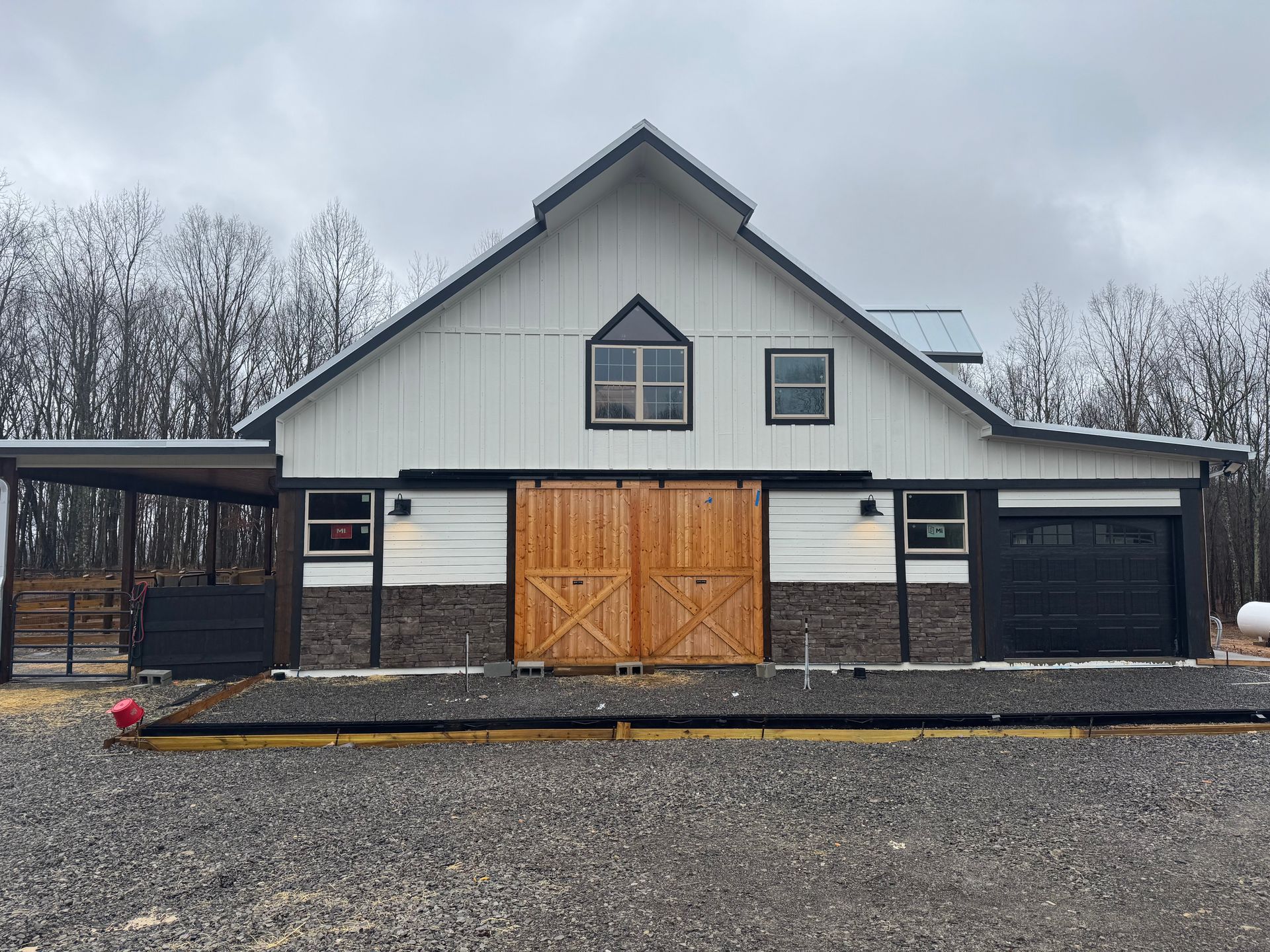 A large white barn with a wooden door is sitting on top of a gravel lot.
