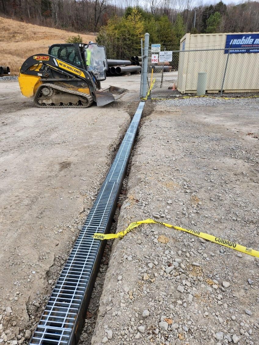 A yellow bulldozer is driving down a gravel road next to a metal grate.
