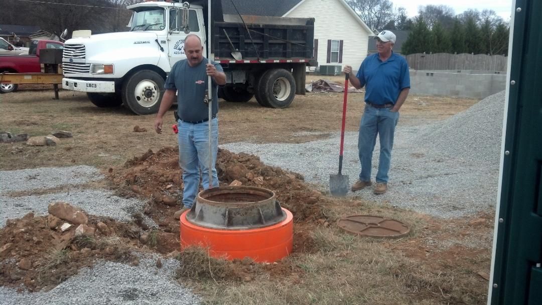 Two men are digging in the dirt in front of a dump truck.