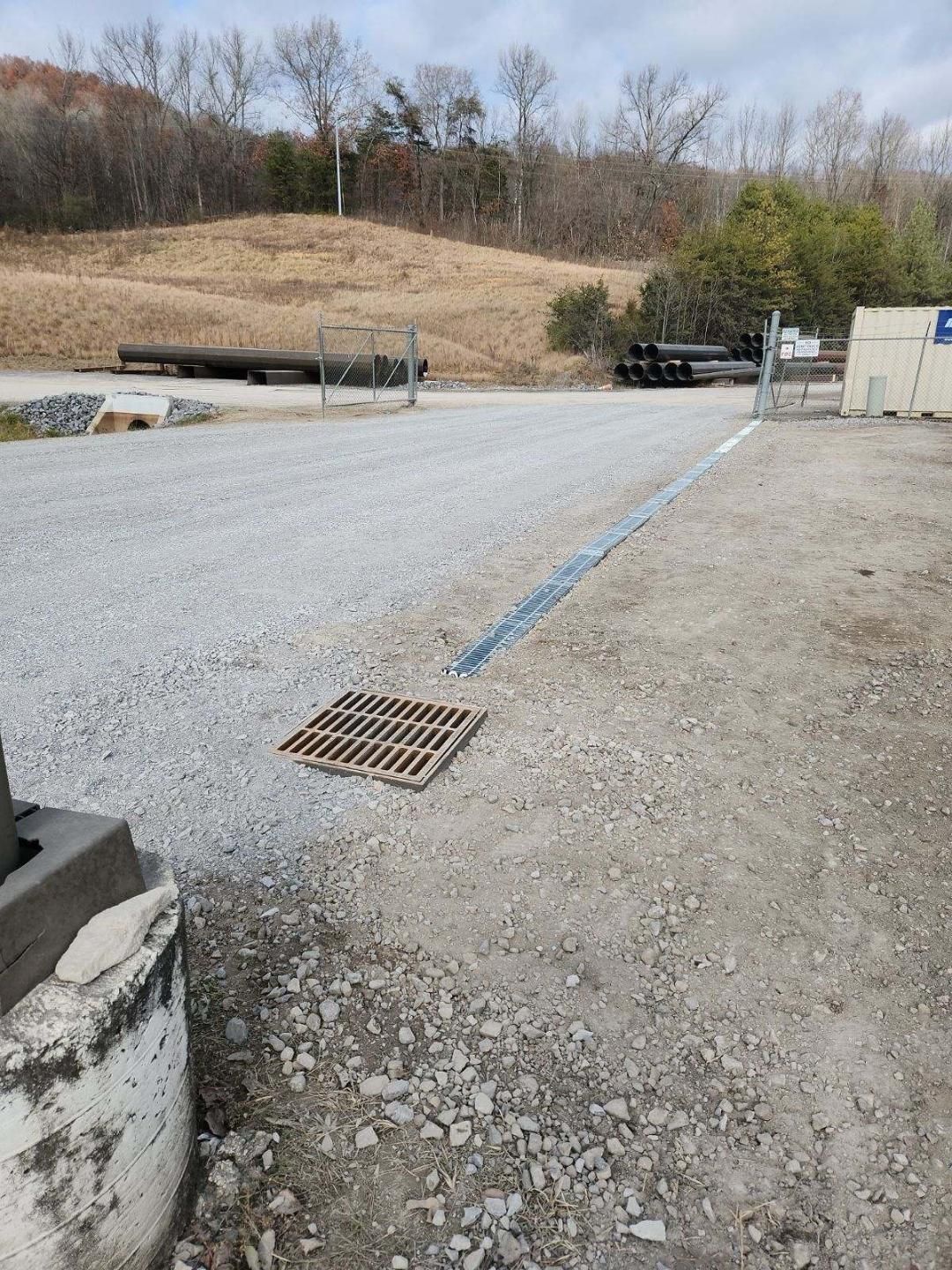 There is a drain on the ground in the middle of a gravel road.