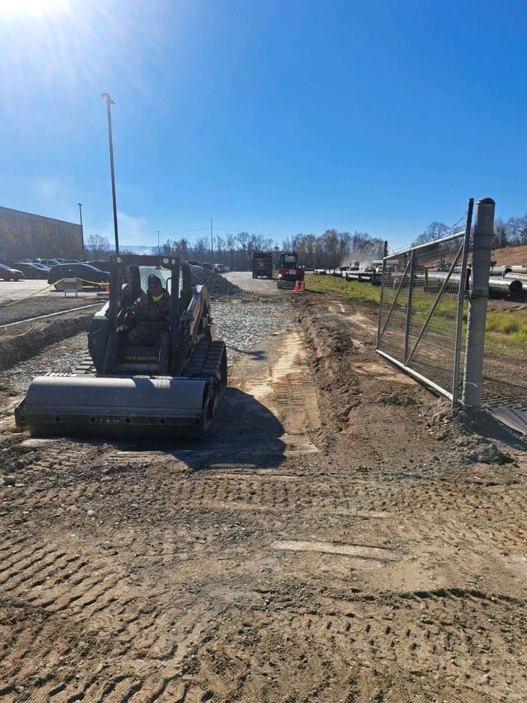 A bulldozer is driving down a dirt road next to a fence.