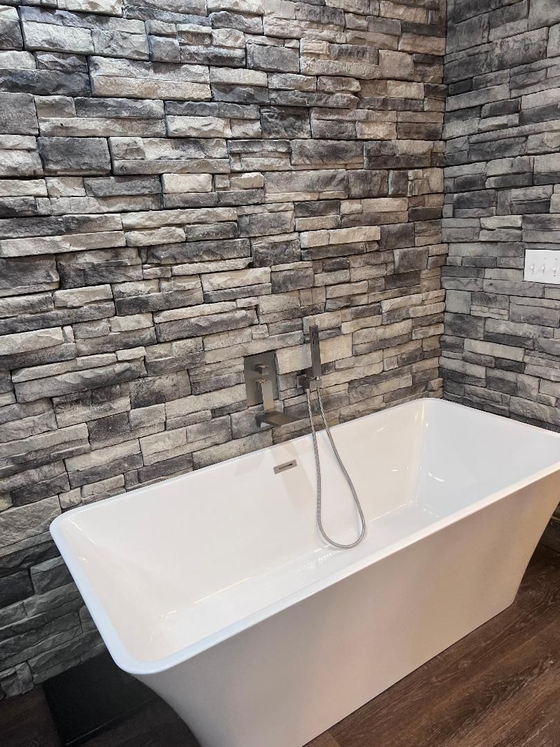 There is a bathtub in the bathroom with a brick wall.