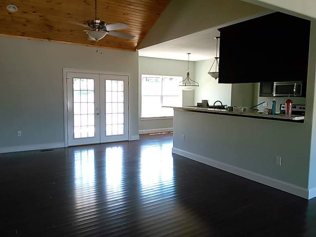 An empty room with a ceiling fan and a kitchen in the background