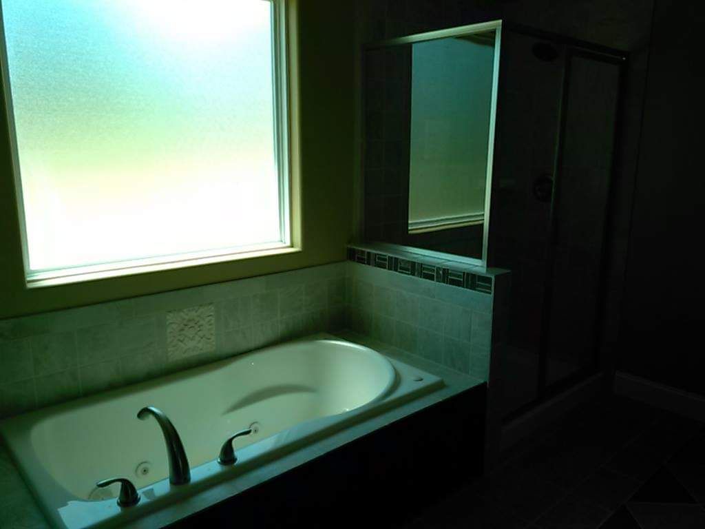 A bathtub in a bathroom next to a window and a mirror.