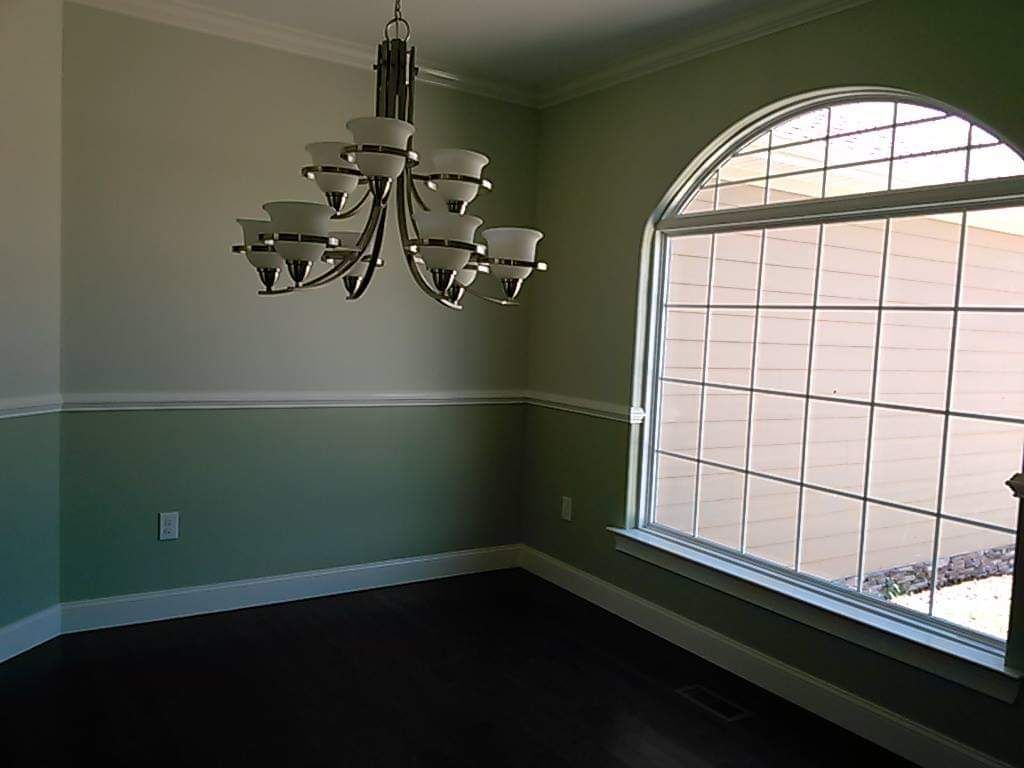 An empty dining room with a chandelier hanging from the ceiling and a large window.