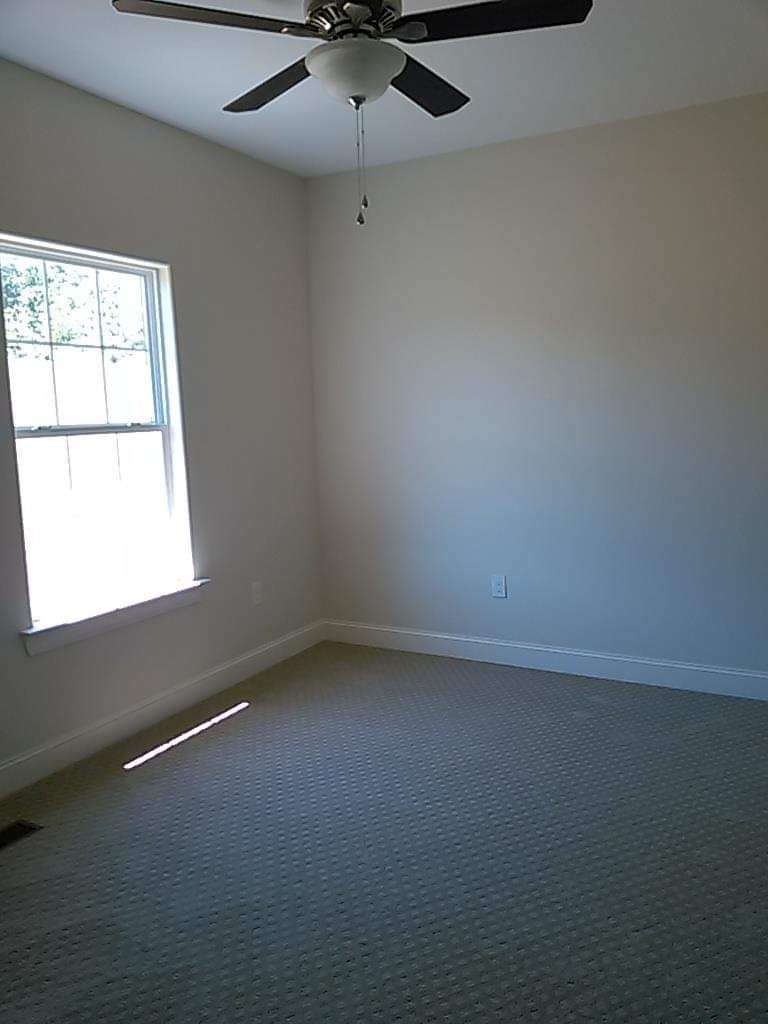An empty bedroom with a ceiling fan and a window.