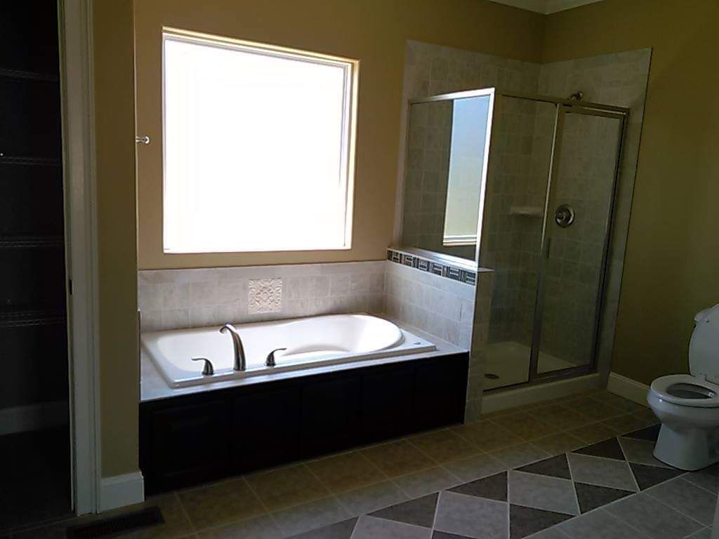 A bathroom with a tub , toilet , shower and window.