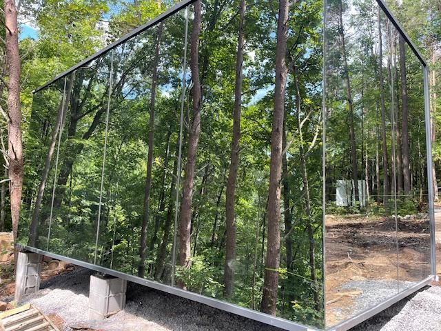A glass building with trees reflected in it is in the middle of a forest.
