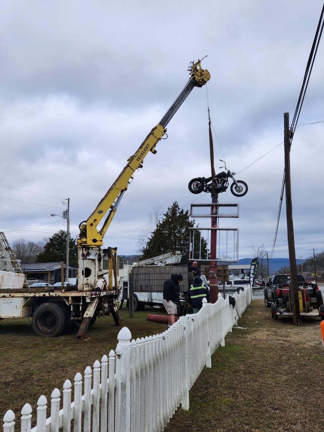 A yellow crane is lifting a motorcycle on top of a sign