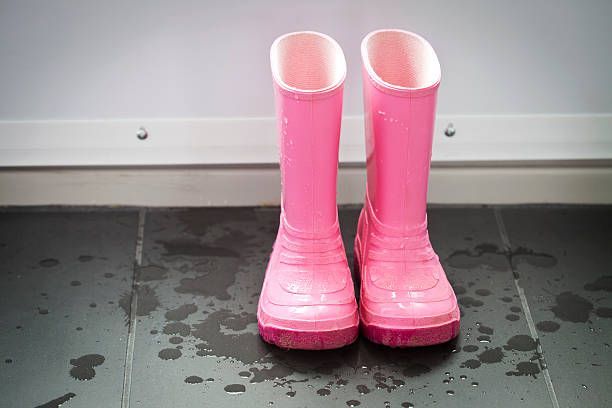 Pink rain boots standing on a wet, dark tile floor.