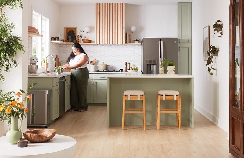 A person washes dishes in a green kitchen with wood accents and a breakfast bar.