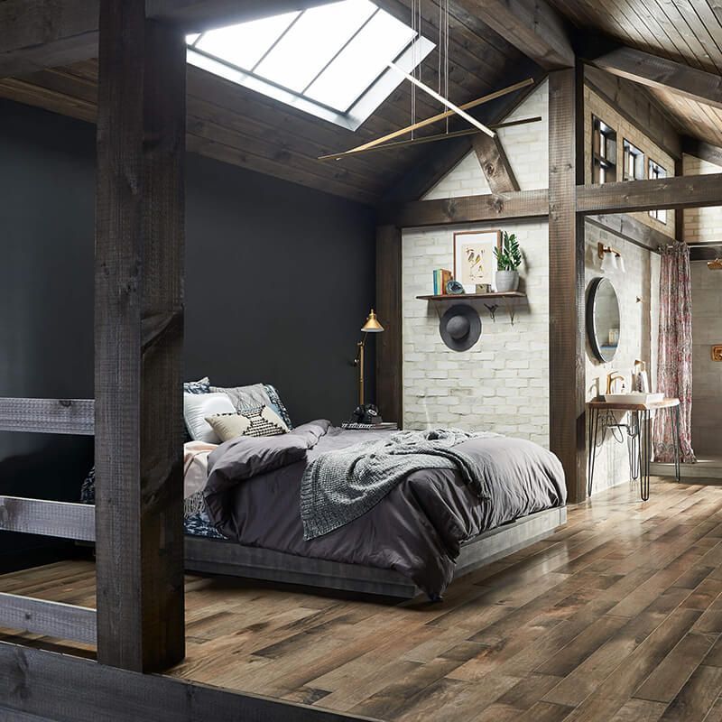 Rustic bedroom with wooden beams, dark walls, bed, and skylight.