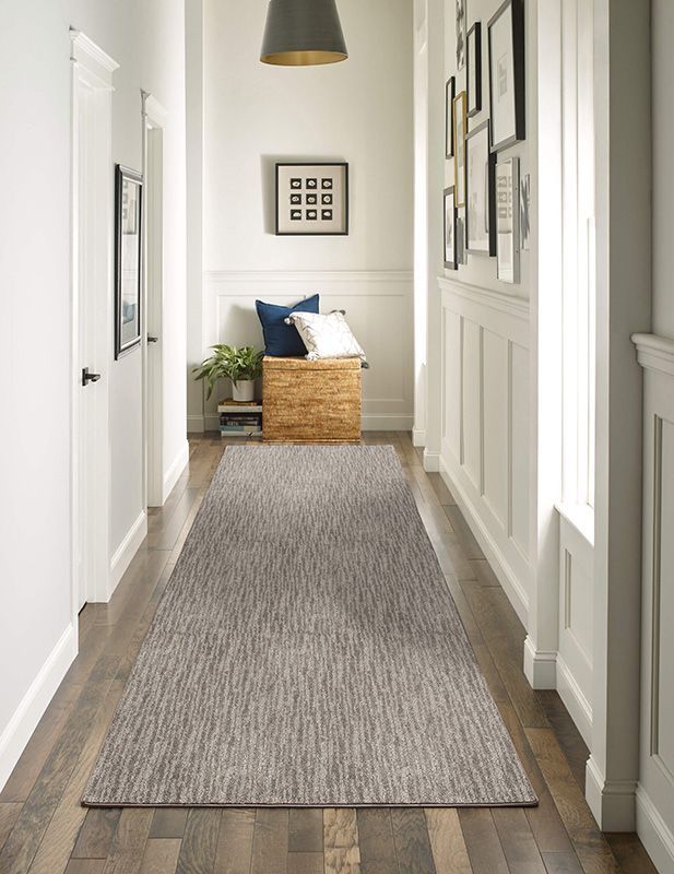 Hallway with wooden floor and textured gray runner rug, white walls, and artwork.