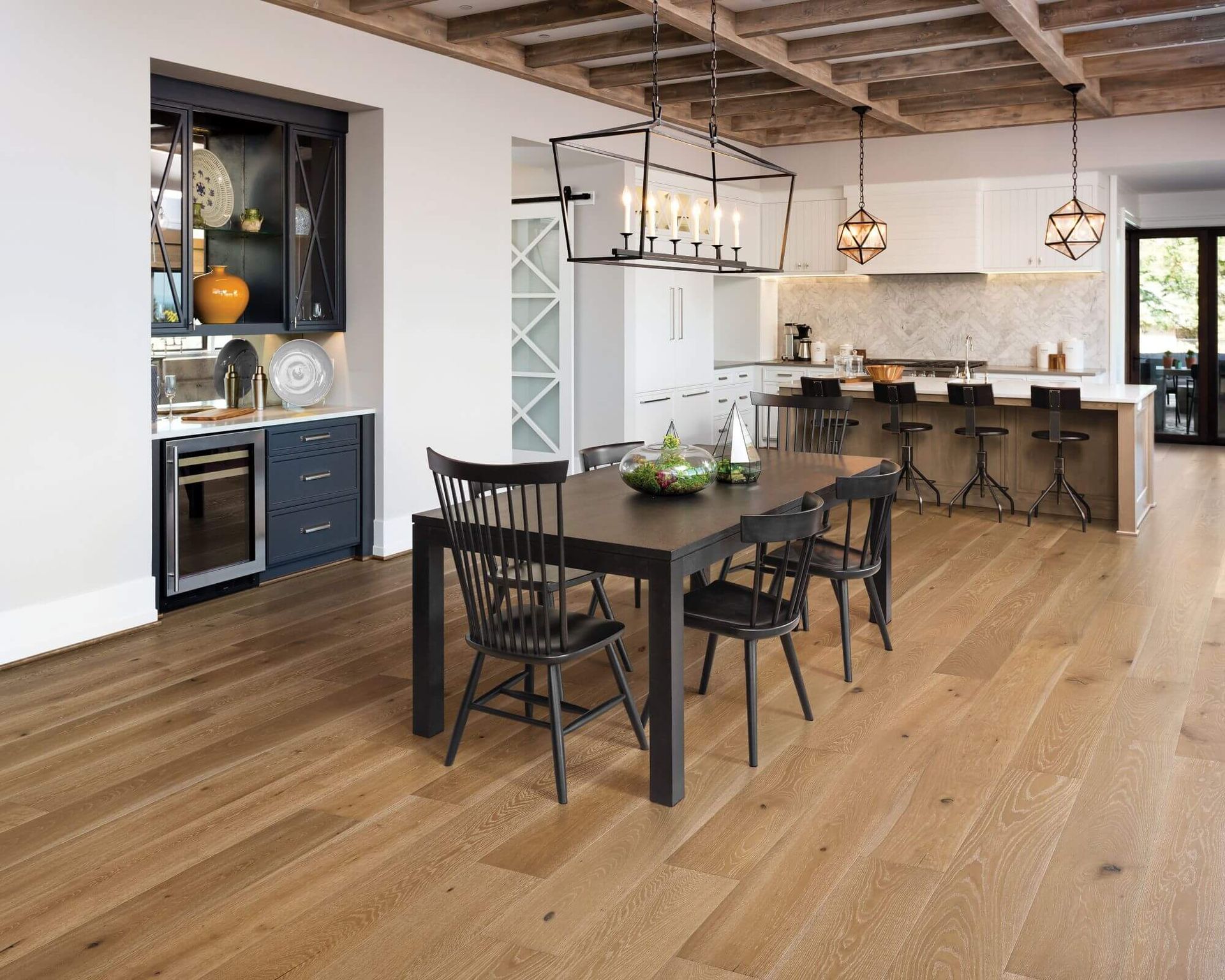 Dining room with wooden floor, dark table and chairs, kitchen in background.