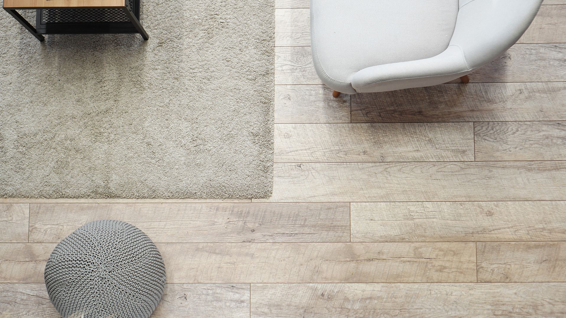 Overhead view of a living room with light wooden floors, a rug, chair, and woven ottoman.