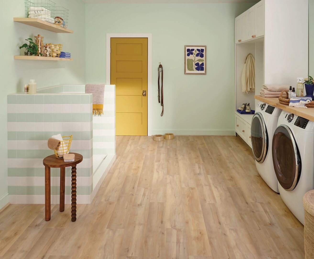 Laundry room with pale wood flooring, mint green walls, and a yellow door.
