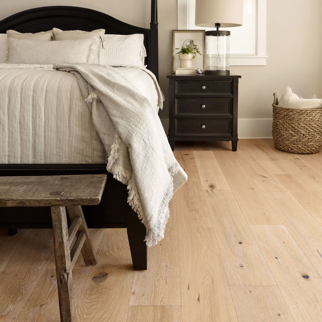 Bedroom with hardwood floor, dark bed, nightstand, and wicker basket, light neutral colors.