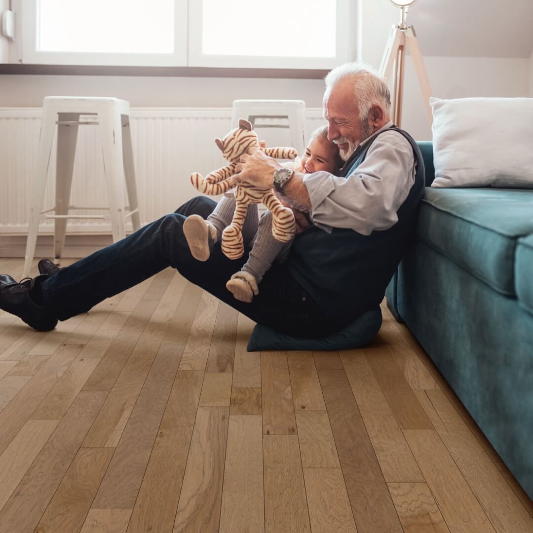 Man sitting on floor hugging child, holding stuffed animal. They are in a living room near a sofa.