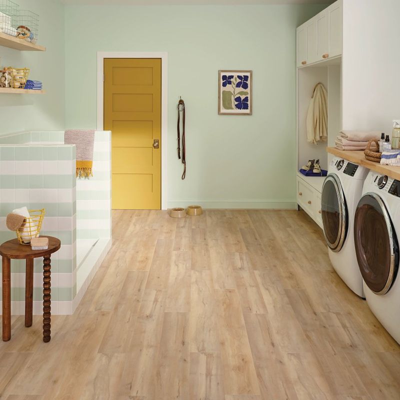 Laundry room with pale green walls, yellow door, and wooden floor. White appliances, storage, and a small table.