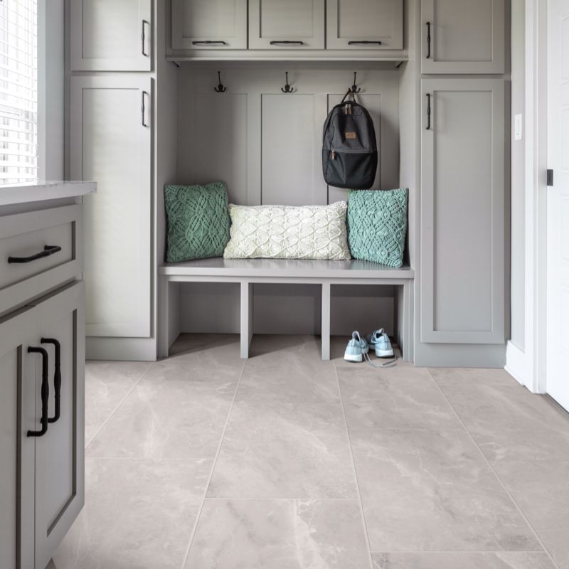A gray mudroom with a bench, cabinets, backpack, and shoes on a light-colored floor.