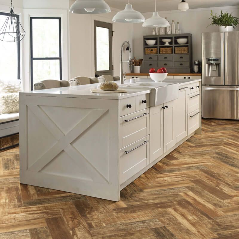 A rustic kitchen with a large white island, farmhouse sink, and herringbone wood floor.