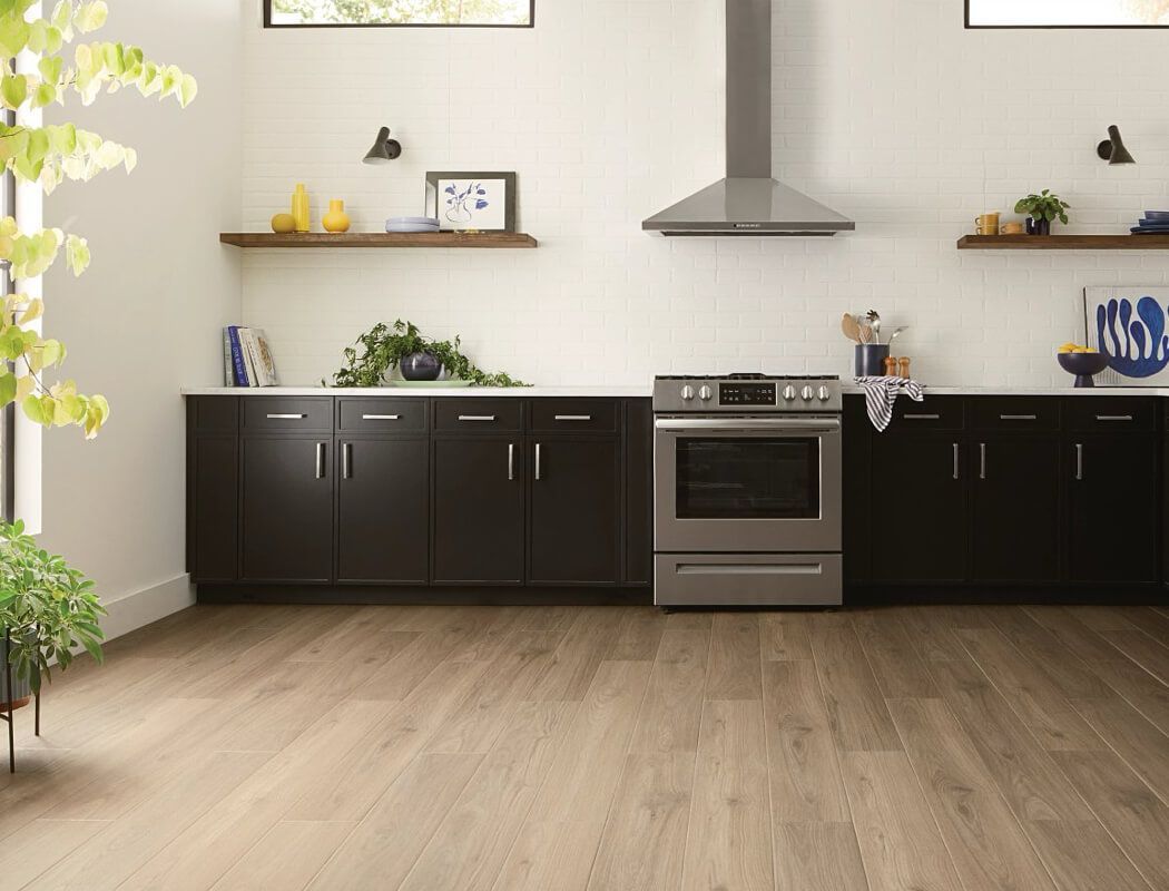 Kitchen with dark cabinets, stainless steel appliances, white walls, and wood-look flooring.