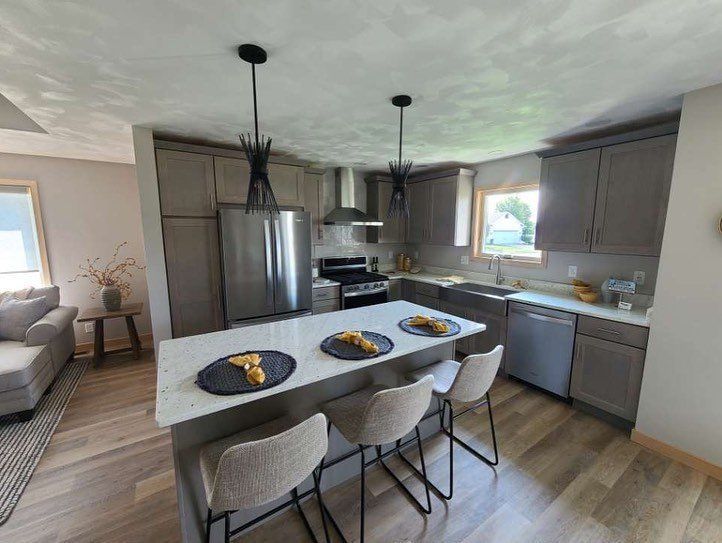 Modern kitchen with gray cabinets, island, stainless steel appliances, and three bar stools.