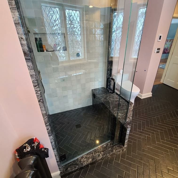 Bathroom with glass shower, black herringbone tile floor, pink walls, and a toilet.