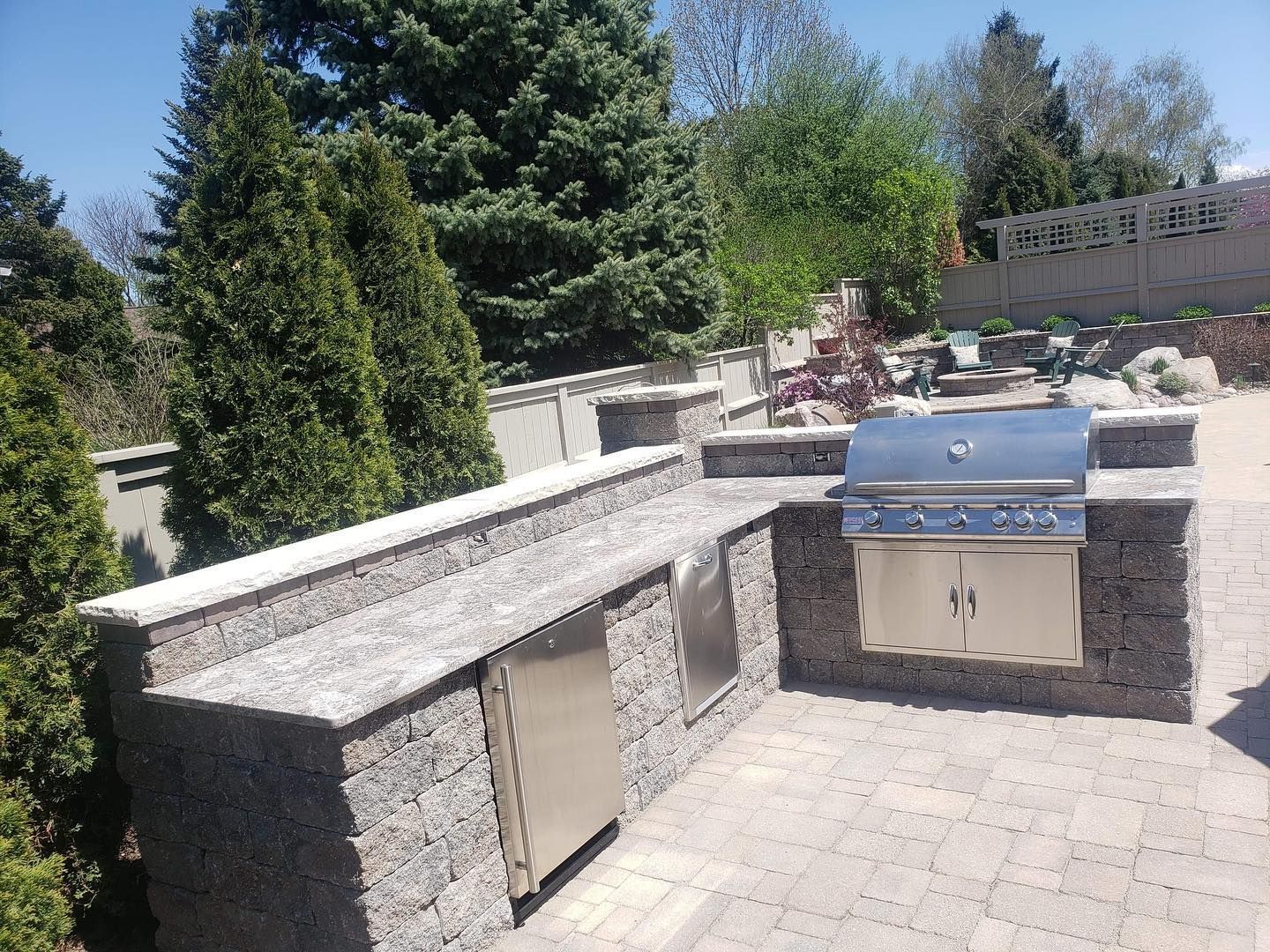 Outdoor kitchen with built-in grill, refrigerator, and countertop on a paved patio.