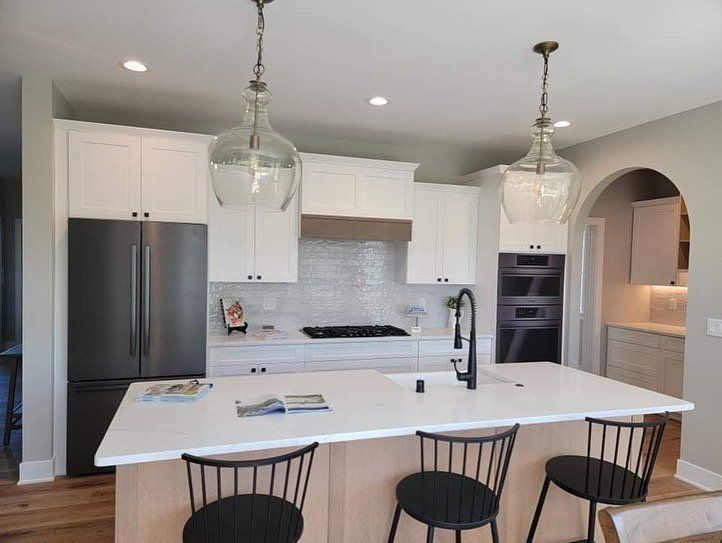 Modern white kitchen with island, stainless steel appliances, and two pendant lights.