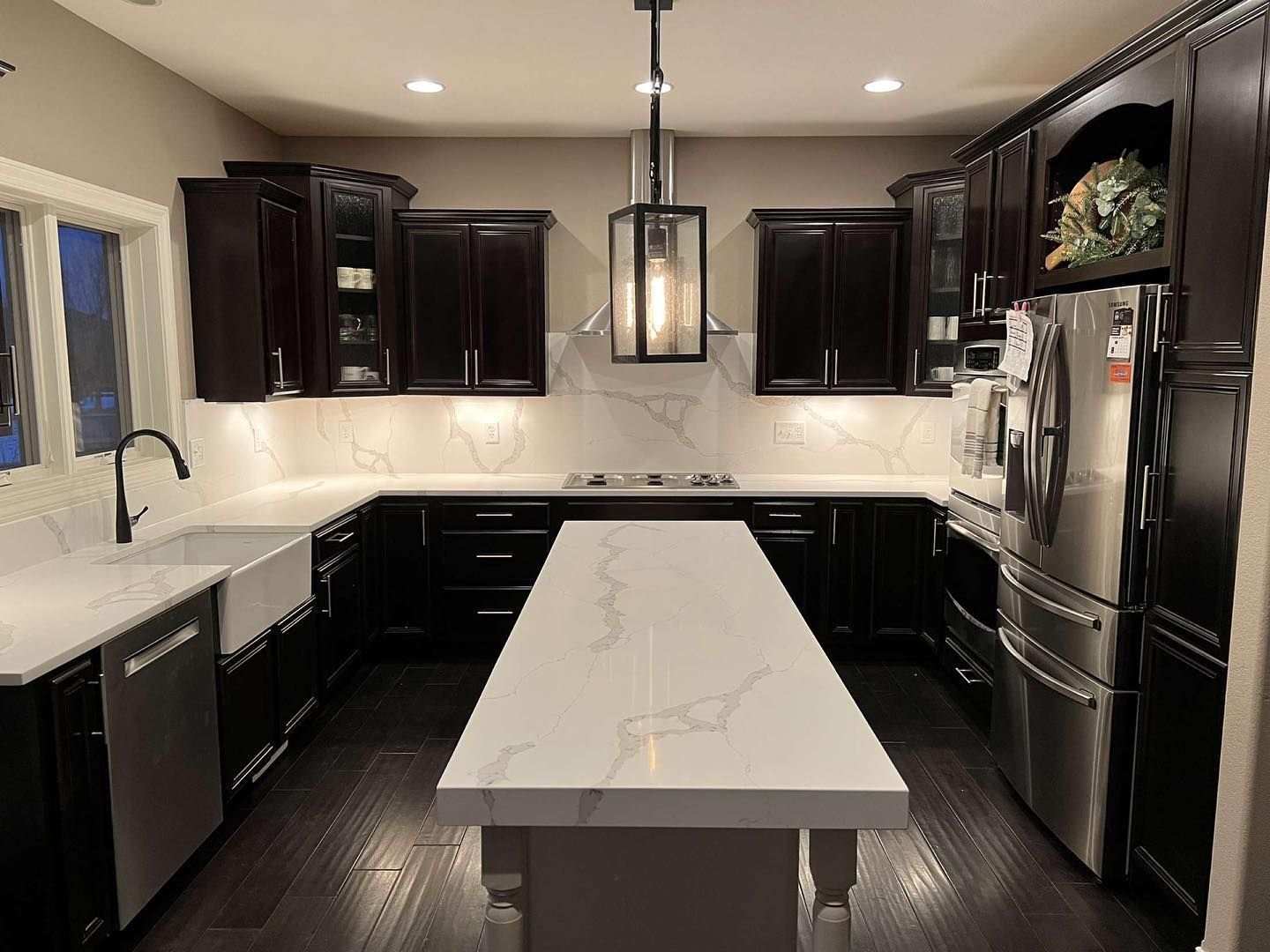 Dark kitchen with white countertops, stainless steel appliances, and dark cabinets.
