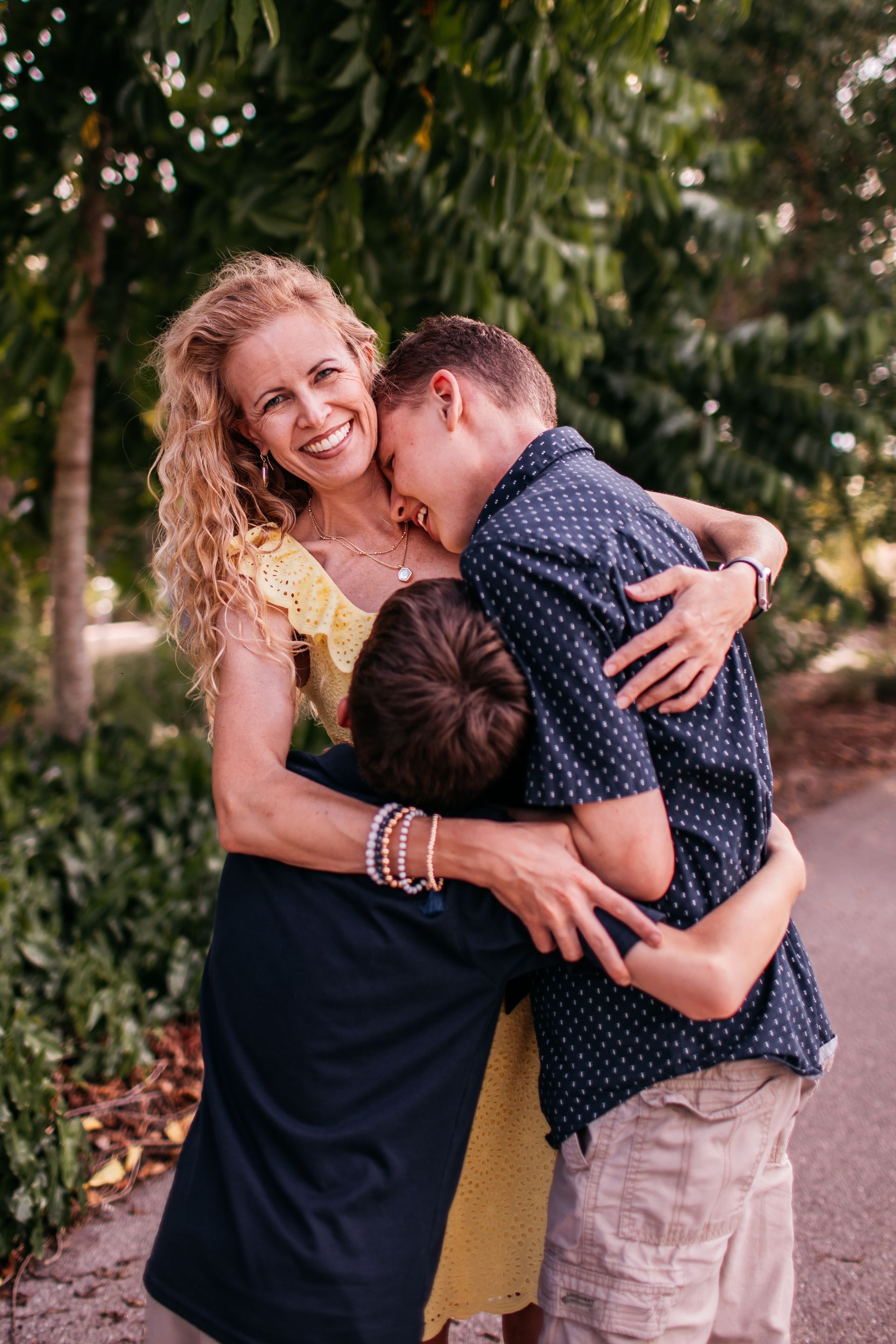 A woman is hugging two boys in a park.