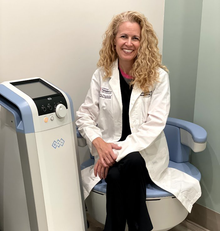 A woman in a lab coat is sitting on a chair next to a machine.