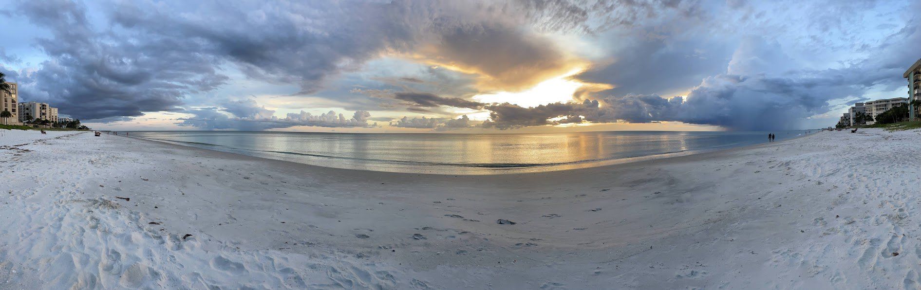 A panoramic view of a beach with a sunset in the background.