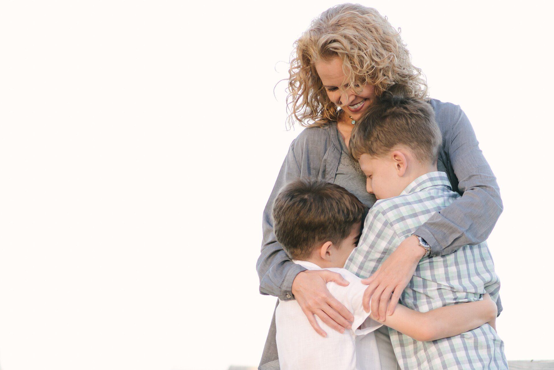 A woman is hugging two boys on a beach.