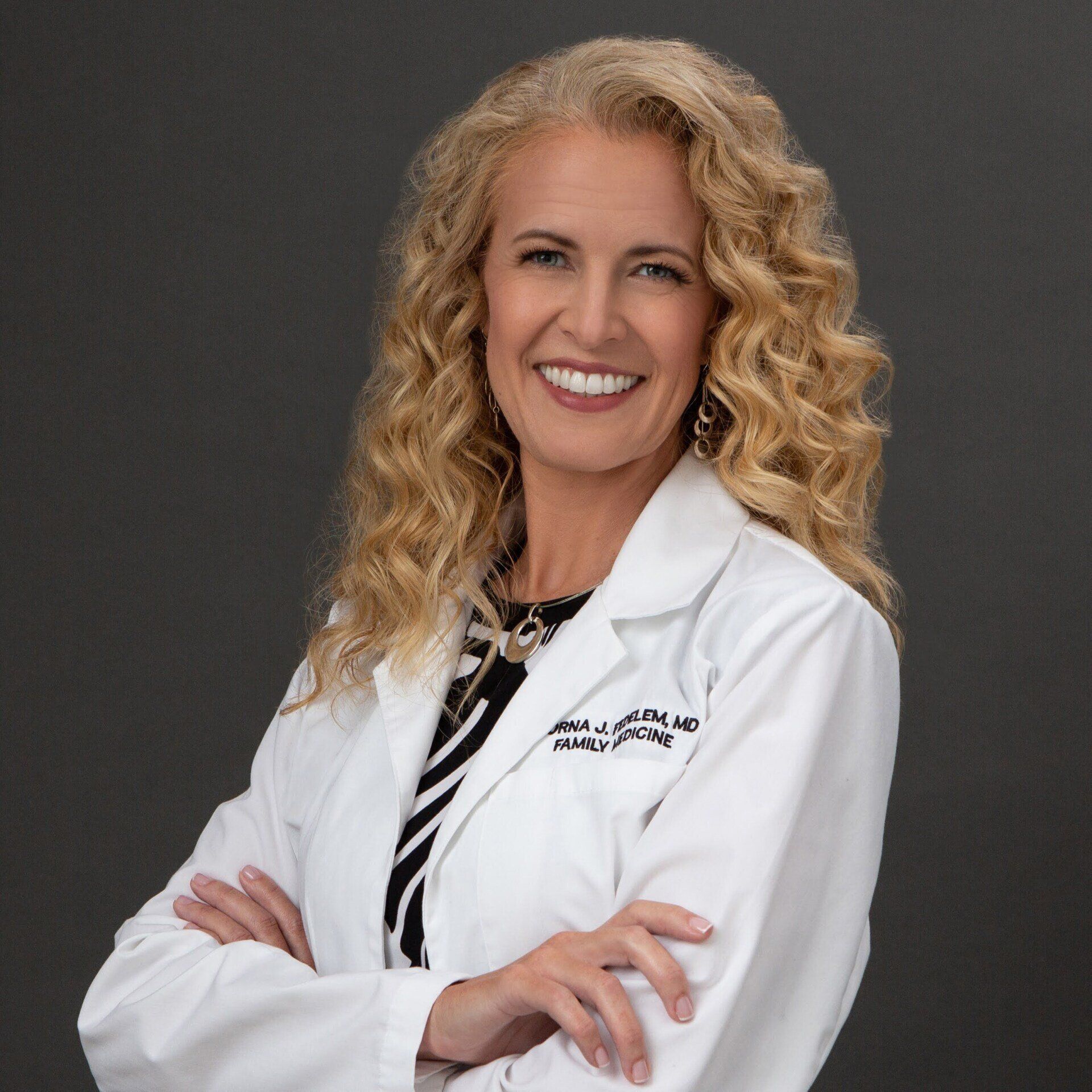 A woman in a white lab coat is smiling with her arms crossed.