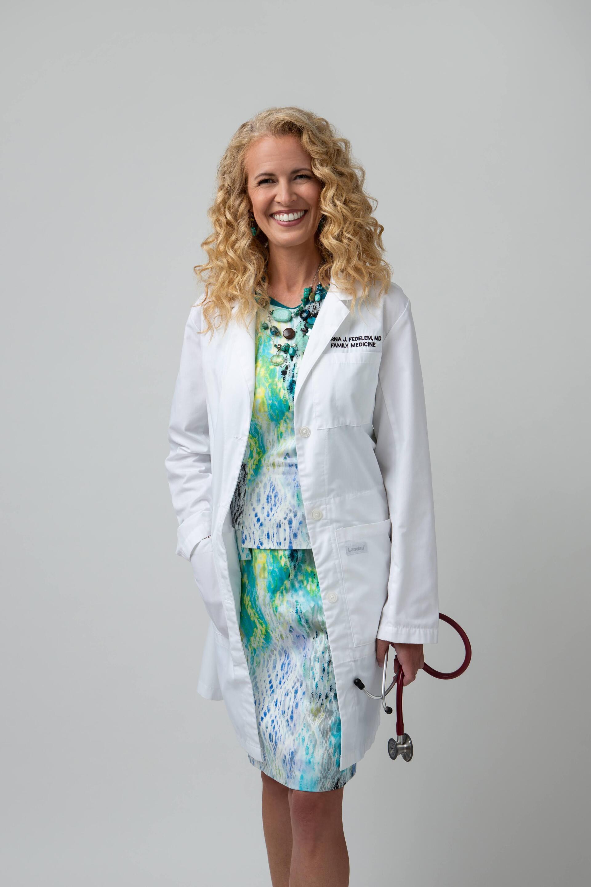 A woman in a white lab coat is holding a stethoscope.