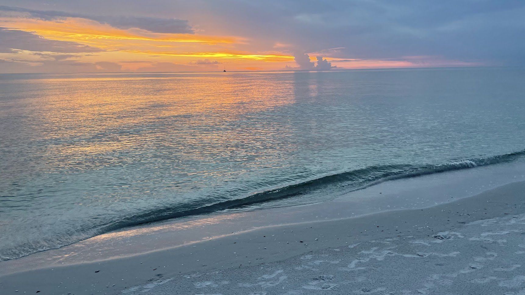 A beach with a sunset in the background and waves crashing on the sand.