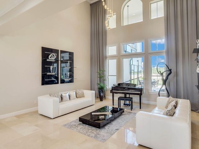 Bright living room with tall windows, white sofas, piano, and a black coffee table on a light rug