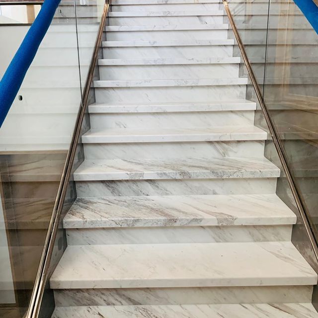 Marble staircase with metal railings and a blue handrail on the left