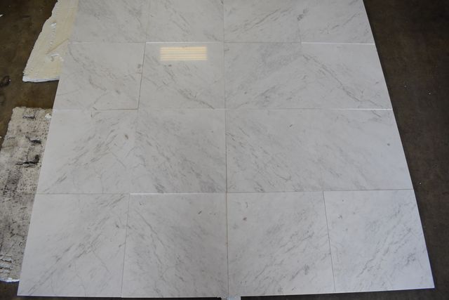 White marble floor tiles laid in a grid, with an unfinished edge on the left.