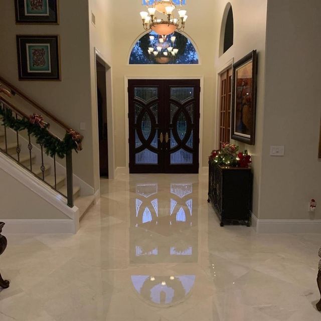 Elegant foyer with glossy marble floors, double front doors, staircase, chandelier, and holiday greenery.
