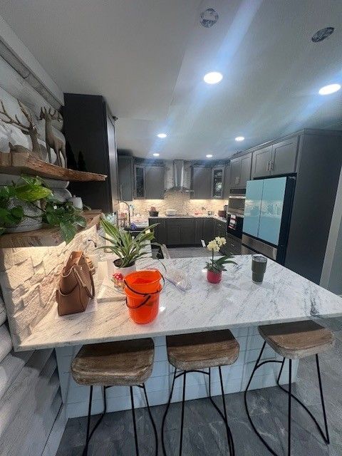 Modern kitchen with marble island, three stools, stainless appliances, and recessed ceiling lights