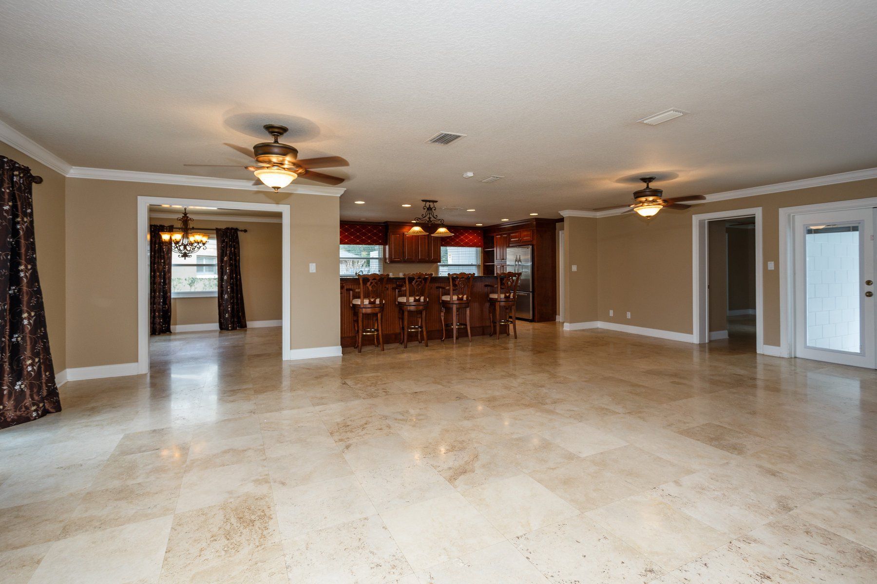 Empty beige living room with tile floor, ceiling fans, and open kitchen area in back