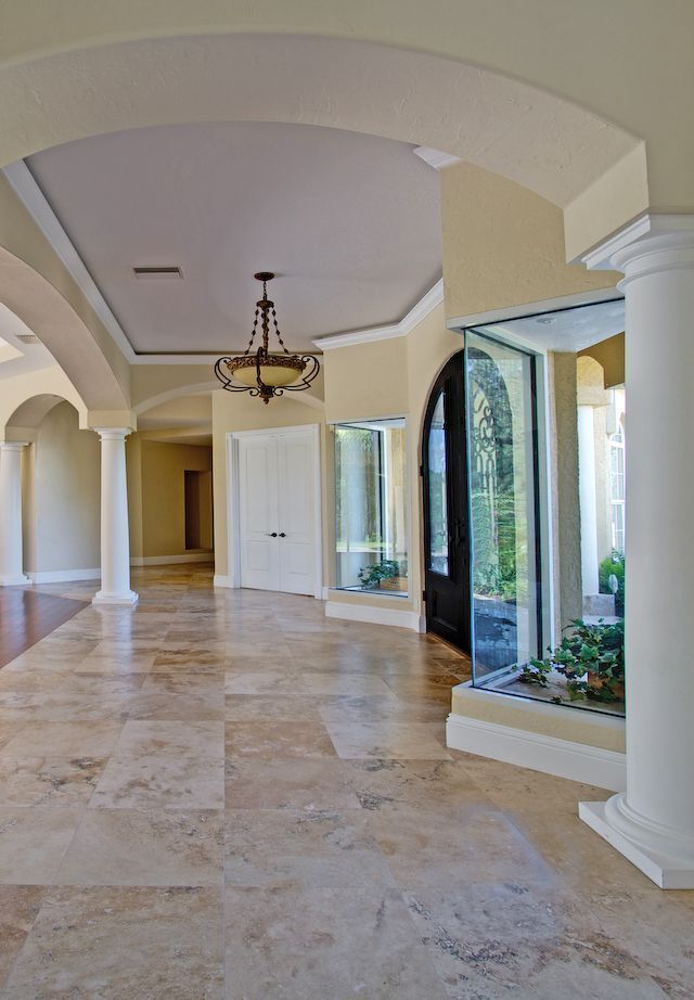 Elegant arched hallway with marble floor, chandelier, and tall windows overlooking greenery