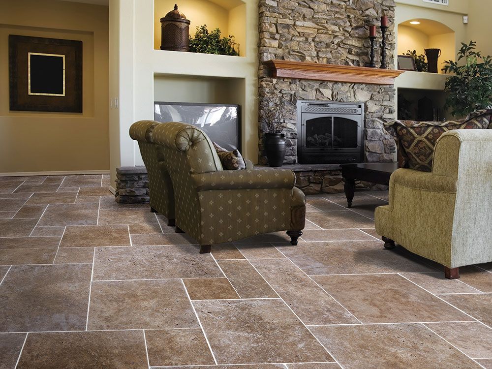 Living room with stone fireplace, beige armchairs, and large brown tile floor